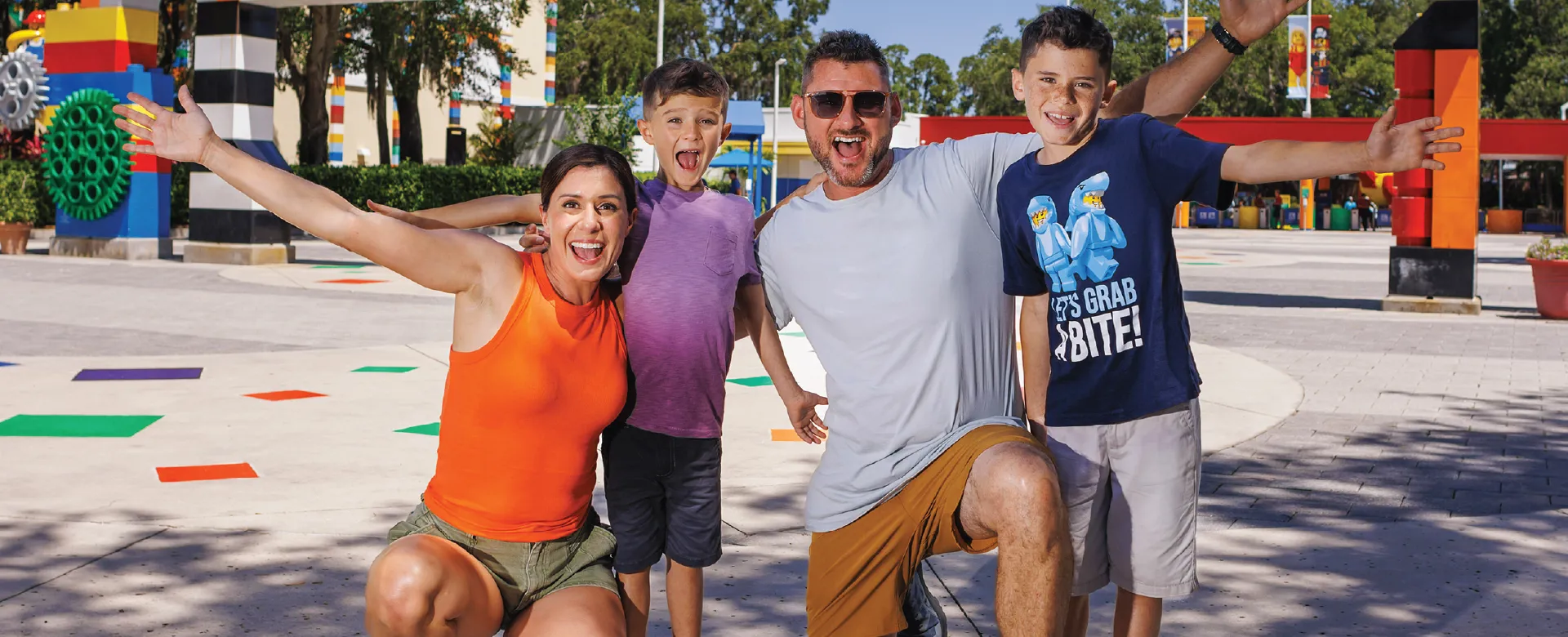 Family of four excitedly posing in front of the colorful LEGOLAND Florida entrance sign.